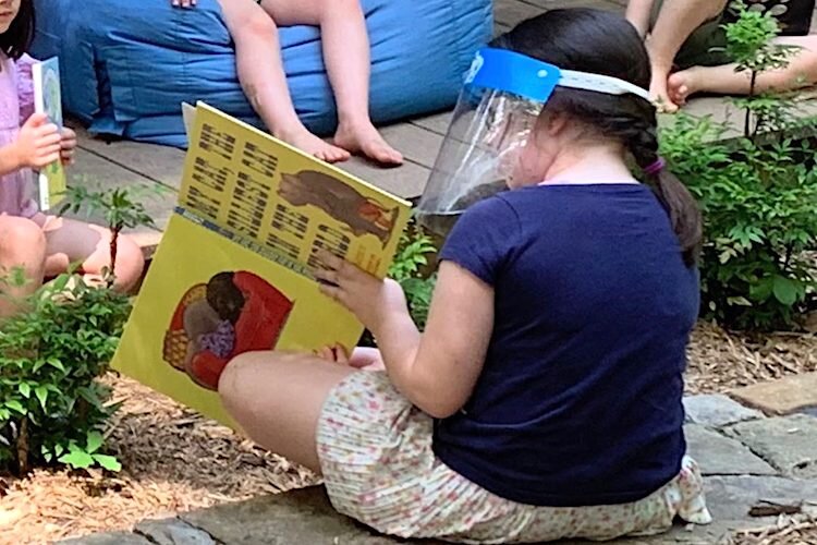 A second-grader reads aloud to preschoolers during summer school.