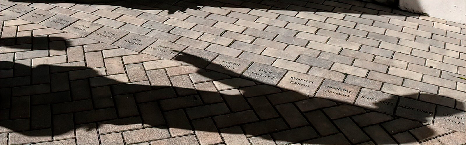 The shadow of historian and guide Fred Hearns as he points to a row of bricks around the church memorializing prominent members and leaders of the African-American community.