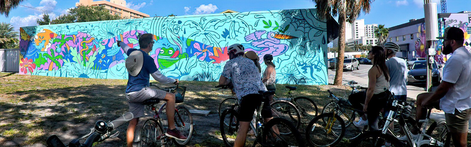 A guide conducting a mural biking tour gives information on the 2023 mural by Nevada artist Hannah Eddy, who wishes to inspire people to appreciate the funkiness in nature.