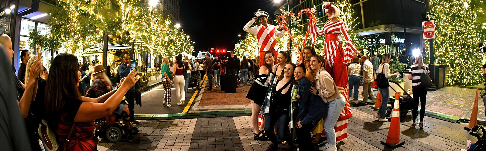 A group of jolly friends gets their picture taken with a backdrop of two candy canes on stilts during Water Street Tampa's annual Season Spectacular event.