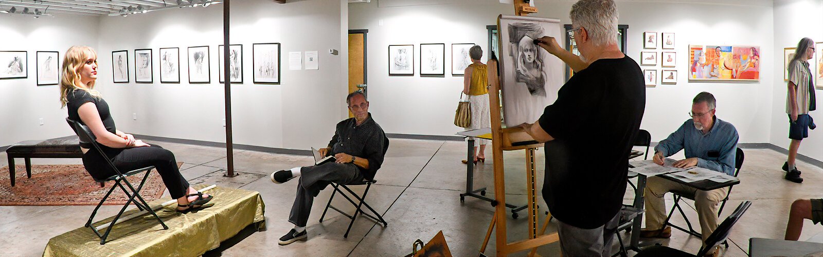 The art show in the Tully-Levine Gallery being a celebration of the human form, portrait artist Jim Kammerud does a live drawing of a young woman while encouraging visitors to draw with him.