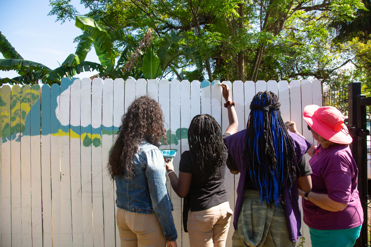 Students with THJCA paint a welcome sign inside the garden space, where they have their own garden plot.