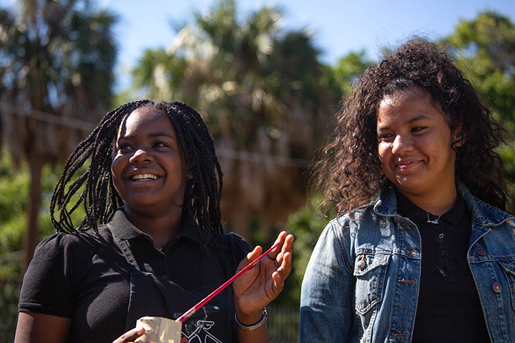 Lifenia Nelson, and Anamarie Ramos watch as friends paint the mural together in Tampa Heights.