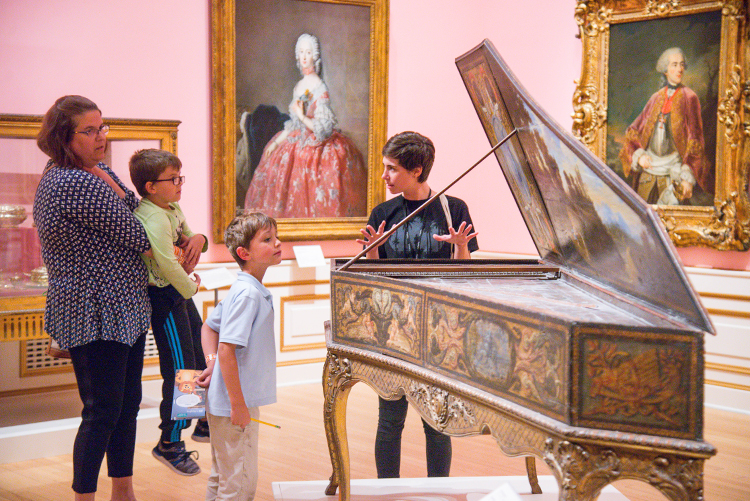 A family examines a harpsichord with a museum educator.