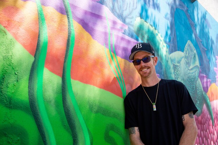 Derek Donnelly of Saint Paint Arts stands with his aquatic mural outside Greenroots Cafe in the Channel District. 