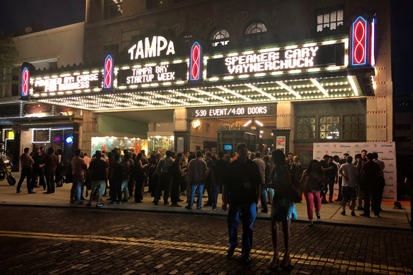 The crowd remains engaged post-speech, outside the theatre.