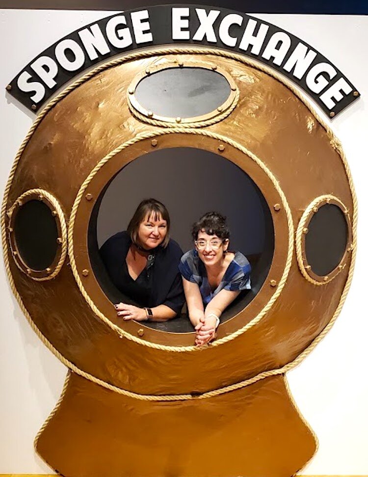 Sarah Howard, USF CAM curator of Public Art and Social Practice, and featured artist Hope Ginsburg pose by a touristy photo stand-in that greets visitors to Ginsburg's Sponge Exchange exhibition at USF CAM.