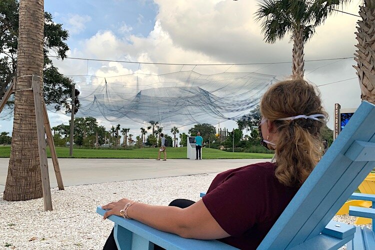 A masked visitor takes a seat to view Bending Arc by Janet Echelman at the new St. Pete Pier.