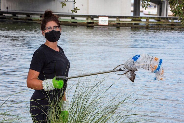 A volunteer uses a handheld clamp to fish wind-blown trash out of the Hillsborough River.