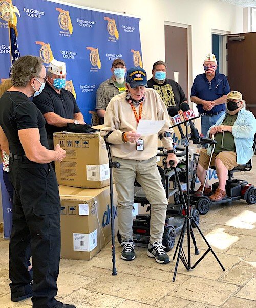 Ray Breault, a Vietnam Veteran, attends the scooter giveaway in his scooter;  Department Commander William ‘Rick’ Johnson is in the background.