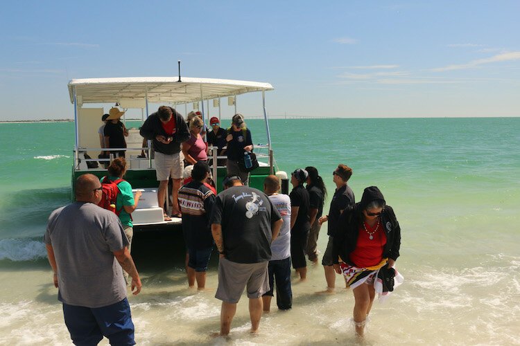 Seminole Tribe members disembark at Egmont Key. The Skyway Bridge is visible in the background.