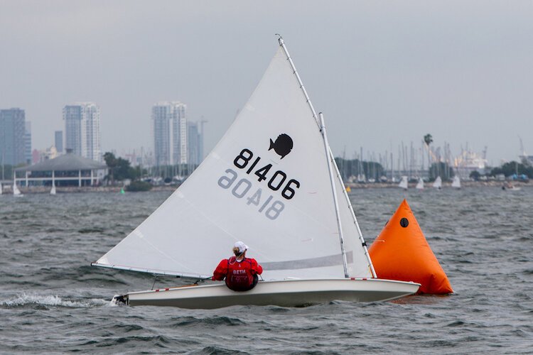 A sailor leans over to keep her Sunfish moving forward in a race with the Tampa downtown skyline in the distance.