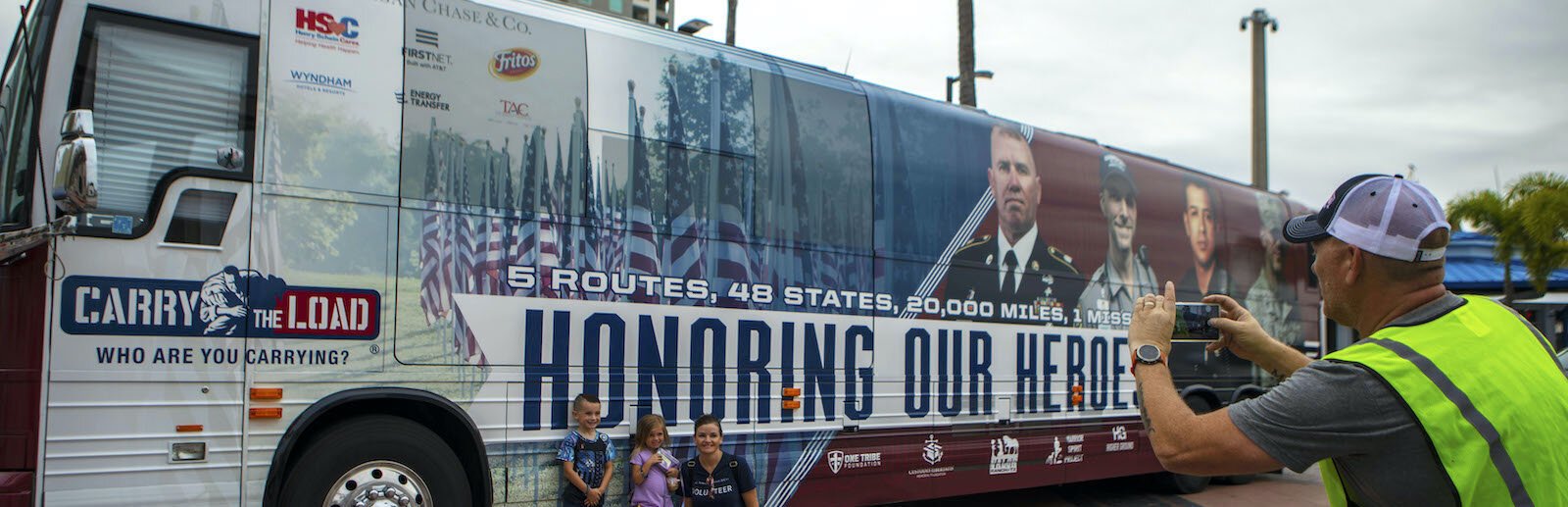 Erin Masciulli, wife of Air Force National Guard Master Sergeant, Eric, along with their children, Eric Jr., 6, and Emma, 4, pose before the non-profit organization "Carry the Load" bus.