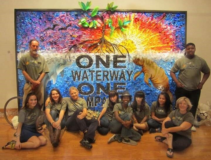Students from Community Stepping Stones pose with  “One Waterway One Tampa Bay,” a mural they made from recyclable materials that is on display at Port Tampa Bay.