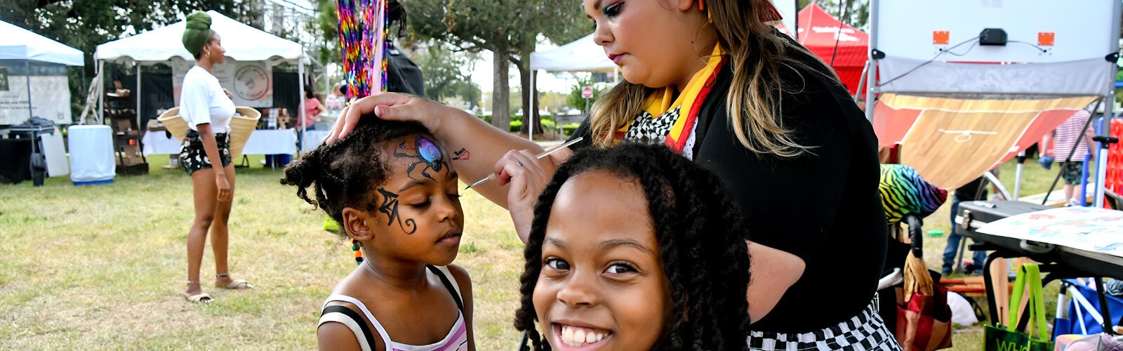 Five-year-old Precious gets her face painted by Lily of “Daisy and Lily’s Face Painting" at the Tampa Bay VegFest as big sister Angel awaits her turn with a big smile of anticipation.