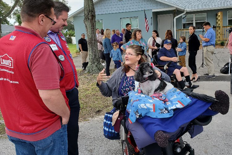 Paula Diviney, with her service dog Ellie Mae, talks with Lowe's representatives, as she waits for the dedication ceremony to her husband, James Diviney, in the wheelchair, is in the background.