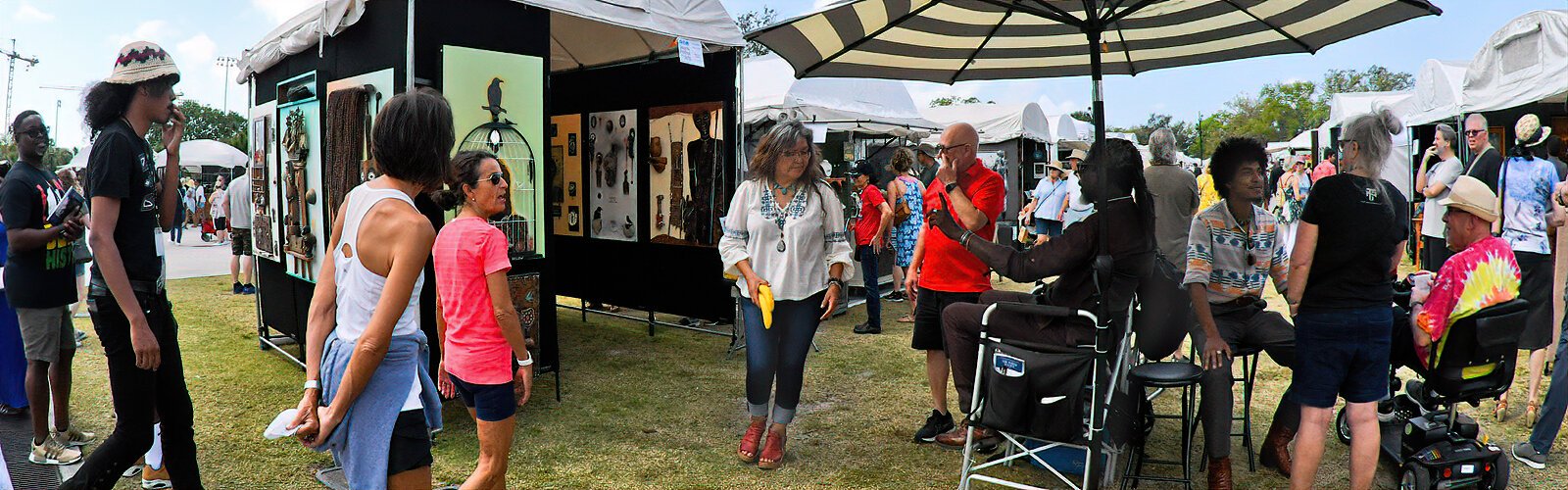 Festival goers interact with artist Athlone Clarke, seated in front of his booth. Athlone's motto is “Art saves lives” and his work of 25 years is collected both nationally and internationally.