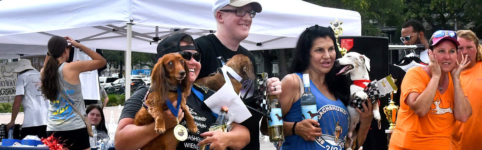 Winners of the Florida Wiener Dog Derby pose for a picture with their humans, displaying medals and prizes won at the running races.