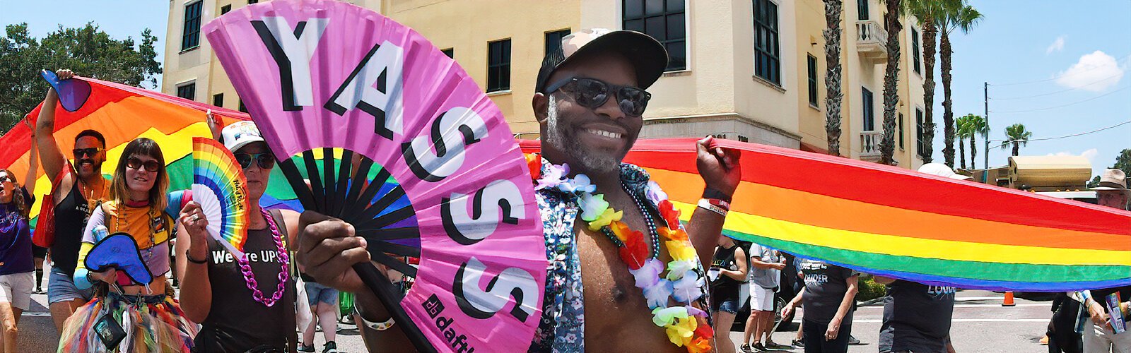 Walking along and holding the ultra-long Pride banner, a festival goer waves a large fan adorned with "Yasss," an excited interjection that means "Yes!" in LGBTQ slang.
