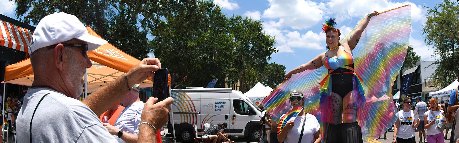 Stilt-walker Maggie Soluna serves as a memorable backdrop for a souvenir photo of St Pete Pride’s street festival.