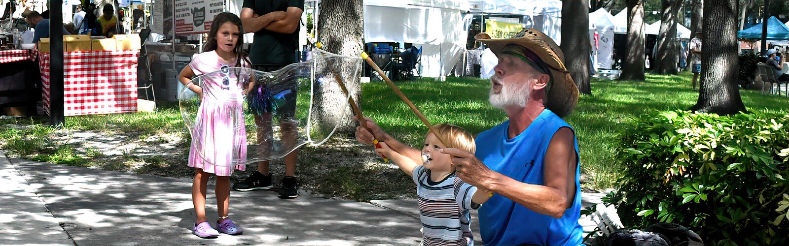 Stiks Bubbleman entertains two young children fascinated by the giant soap bubbles he makes with his bubble sticks at the Saturday Morning Market.