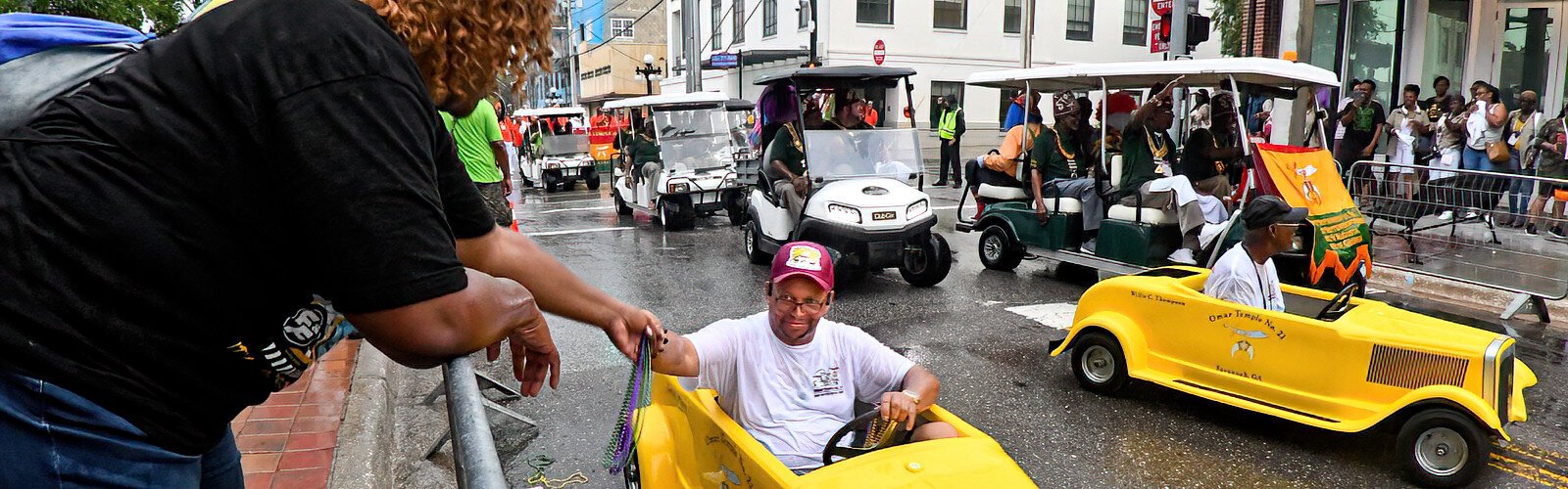 A member of the Omar Temple No. 21 from Savannah GA. hands out beads to a parade watcher from his tiny yellow vehicle, an entertaining distinction special to the Shriners.