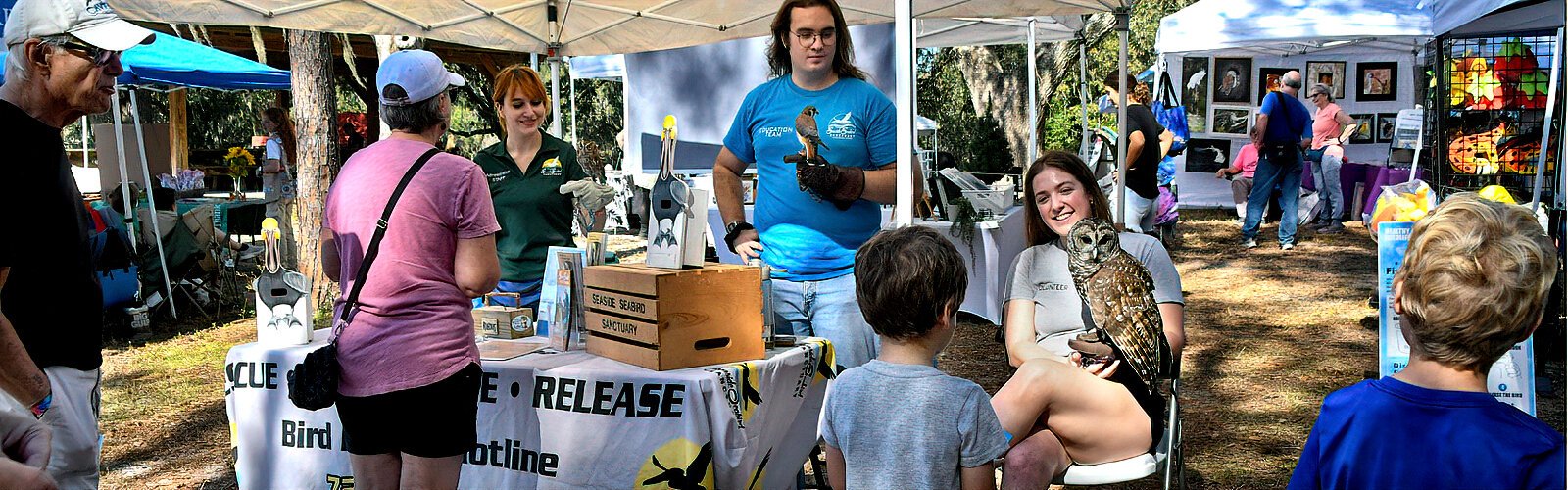 The wildlife rehabilitation facility Seaside Seabird Sanctuary educates festival goers with Mikaella and barred owl Pacino, Daniel with American kestrel Kevin and Keegan with screech-owl Rufous.