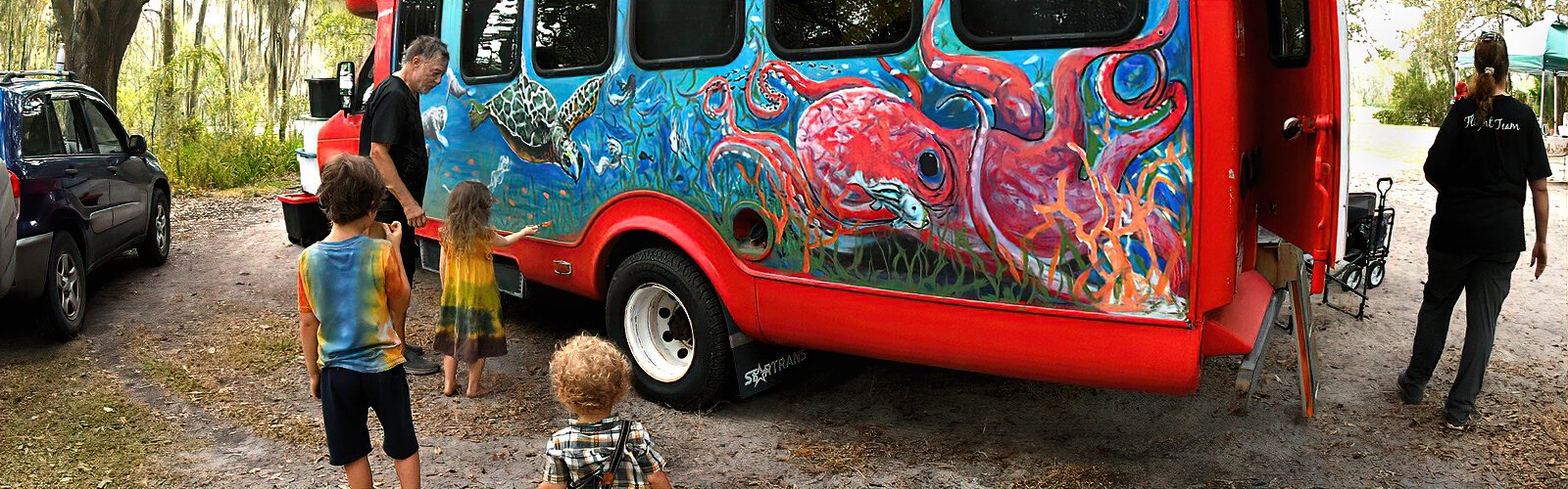 Muralist Terry Klaaren encourages a little girl to paint a few fish on the marine life mural he’s creating on the Raptor Center’s Magical Bird Bus.