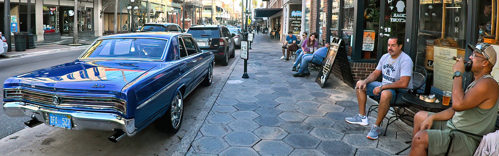  A cigar lover relaxes with another aficionado outside La Faraona Cigar Lounge while keeping an eye on his immaculate 1965 Buick Skylark antique car.