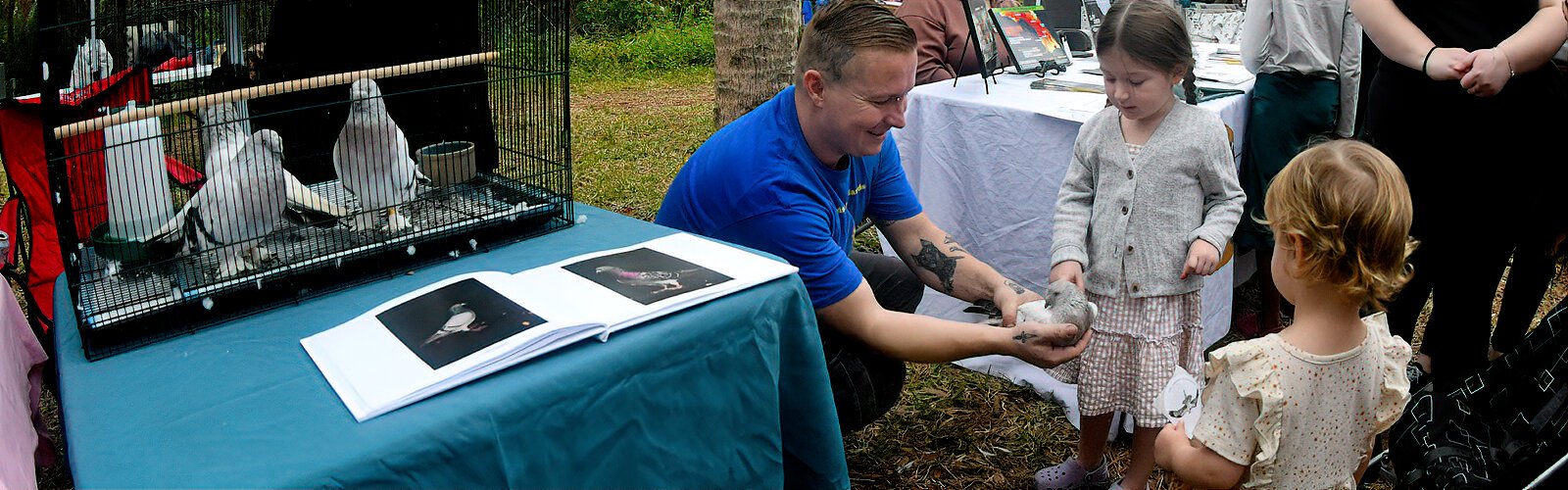 Pigeon foster Joe Sharp encourages Nora, 3, to pet a so-called “fancy pigeon.” These unusual pigeons were abandoned in a church, rescued by BHH and are now housed by Sharp.
