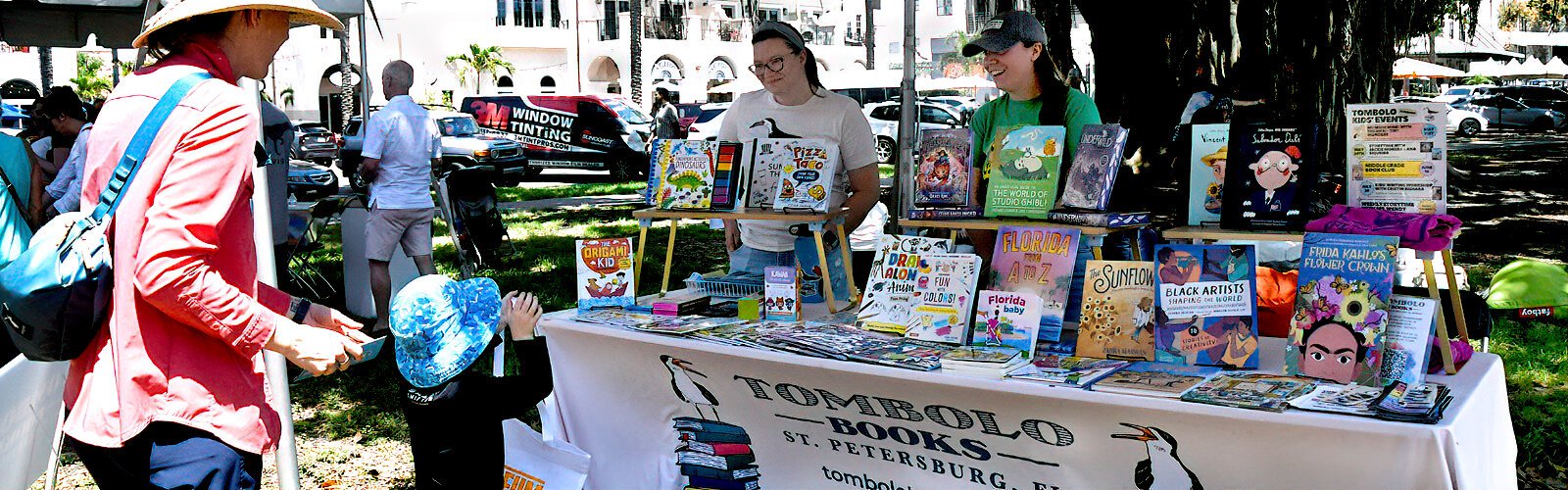 Joanna and Kelsey from St. Pete’s Tombolo Books interact with a little boy curious about their selection of children’s books.