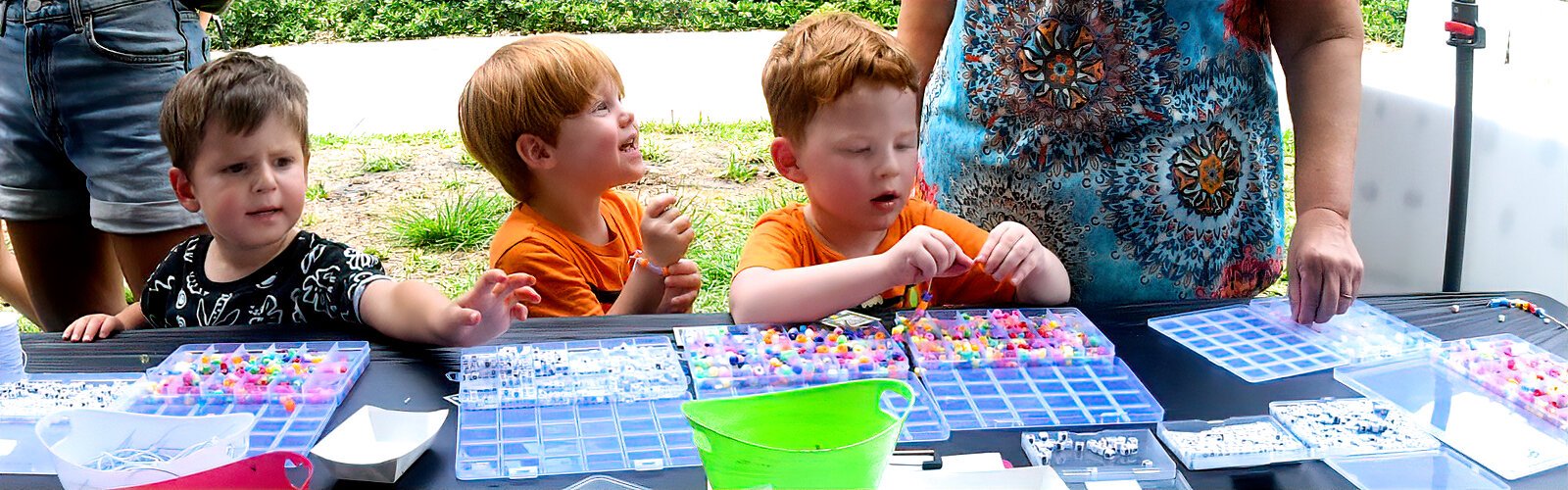 At this Painting in the Park activity booth, twins Jackson and Gavin, 3, enjoy stringing beads and making bracelets.