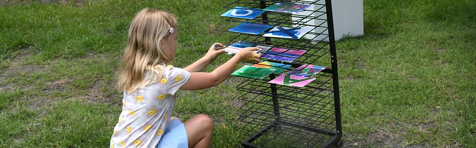 Charley, 7, carefully places her artwork on the drying rack at Painting in the Park’s “peel and reveal” art station.