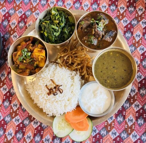 Thakali thali set - a traditional platter featuring rice, lentils, pickles, vegetables, and meat curry (often goat or chicken).