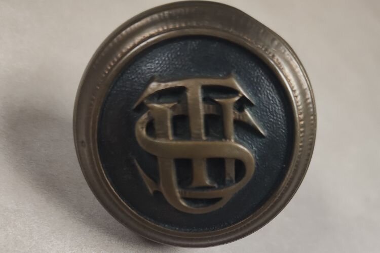 An original 1912 doorknob from Tampa Union Station, featuring the station's logo, with the intertwined "TUS."
